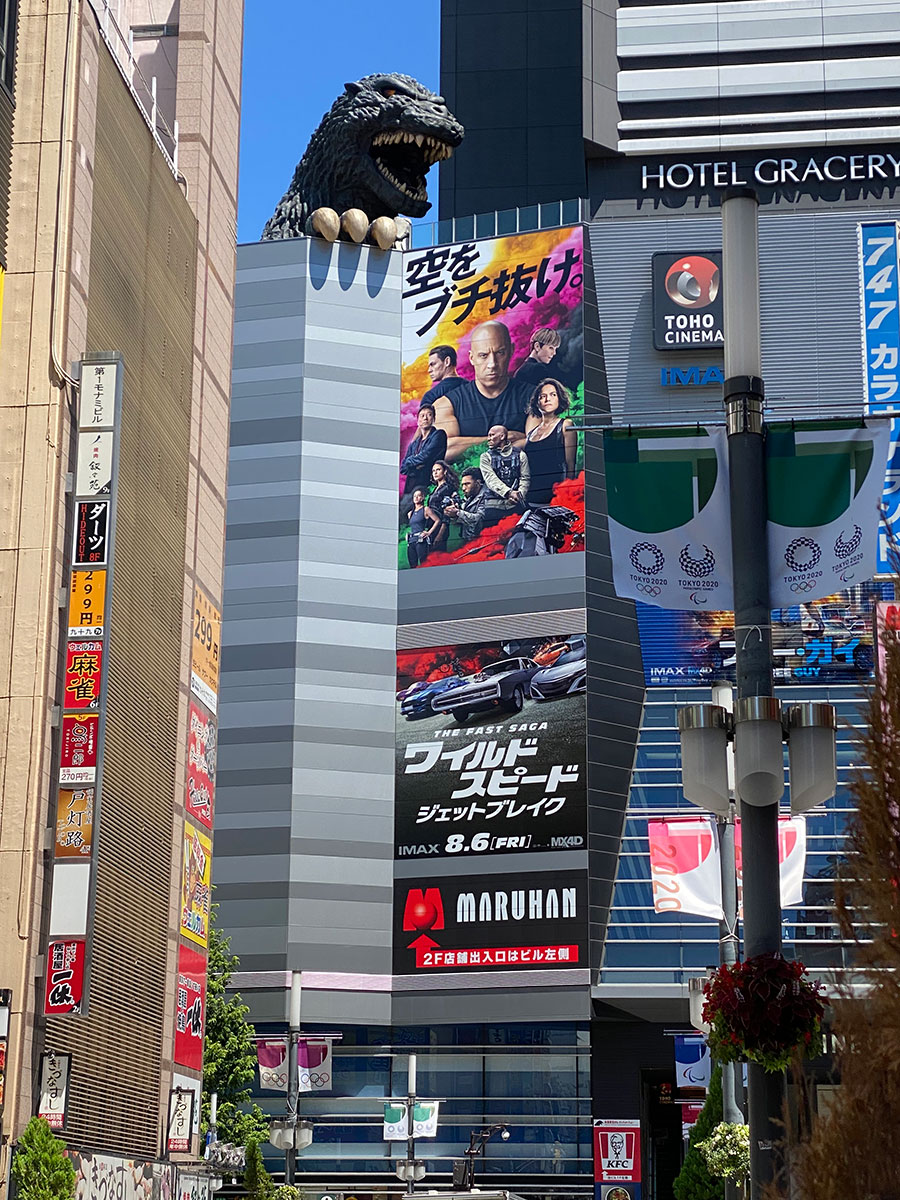 TOHOシネマズ新宿が入っている新宿東宝ビル壁面に飾られた『ワイルド・スピード／ジェットブレイク』キーヴィジュアルと、それを見下ろすゴジラヘッド。